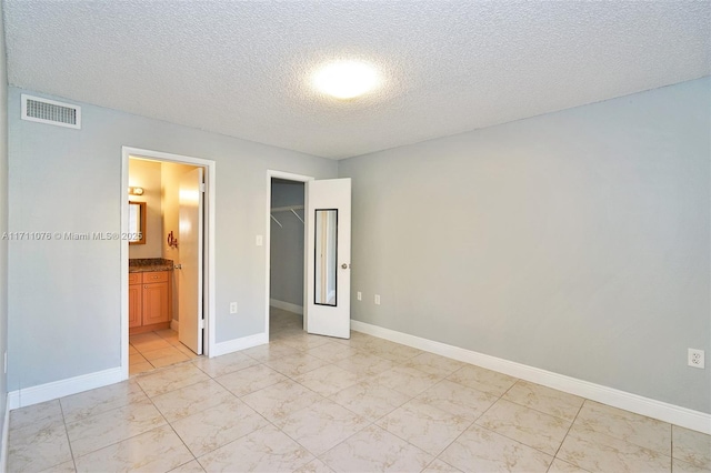 unfurnished bedroom with ensuite bathroom, a walk in closet, a textured ceiling, and a closet