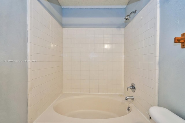 bathroom with tiled shower / bath combo, a textured ceiling, and toilet