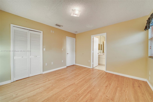 unfurnished bedroom featuring a closet, a textured ceiling, connected bathroom, and light hardwood / wood-style flooring