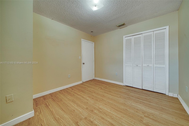 unfurnished bedroom with light wood-type flooring, a textured ceiling, and a closet