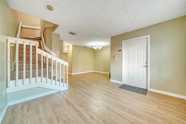 empty room with a notable chandelier, a textured ceiling, and light hardwood / wood-style flooring