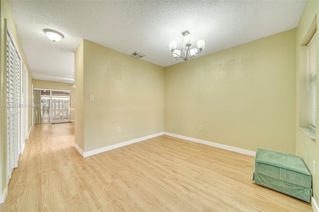 spare room with light hardwood / wood-style flooring, a textured ceiling, and an inviting chandelier