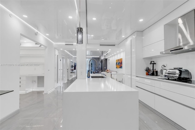 kitchen with wall chimney exhaust hood, white cabinetry, sink, and a kitchen island