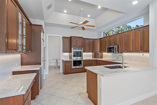 kitchen with light stone countertops, tasteful backsplash, kitchen peninsula, a tray ceiling, and appliances with stainless steel finishes