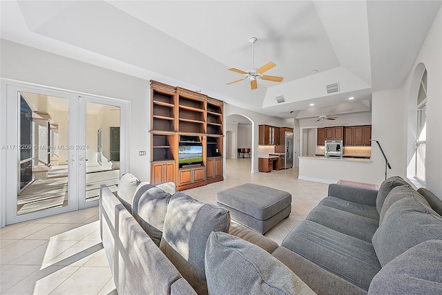 tiled living room with ceiling fan, a raised ceiling, french doors, and built in shelves