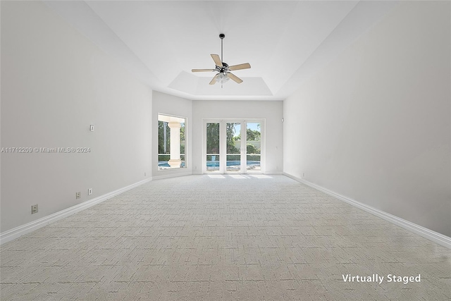 unfurnished living room with a raised ceiling, light carpet, and ceiling fan