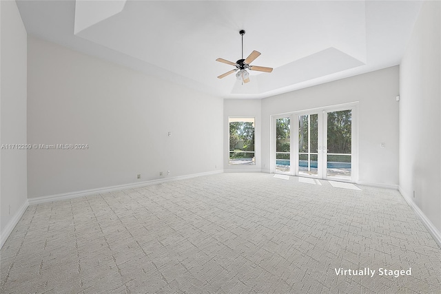 empty room with ceiling fan, light carpet, and a tray ceiling