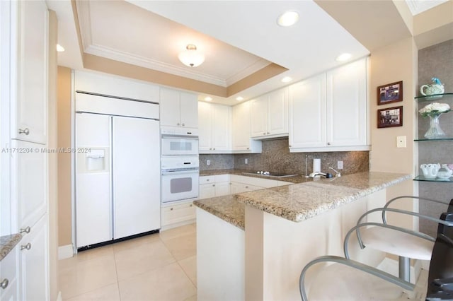 kitchen featuring white cabinetry, light stone countertops, kitchen peninsula, white appliances, and a kitchen bar