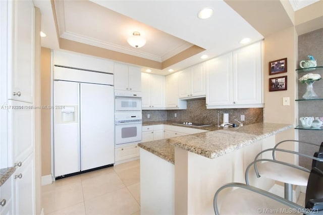 kitchen with white appliances, a kitchen breakfast bar, kitchen peninsula, light stone countertops, and white cabinetry