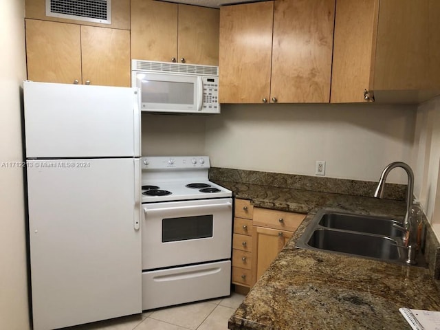 kitchen featuring sink, light tile patterned floors, dark stone counters, and white appliances