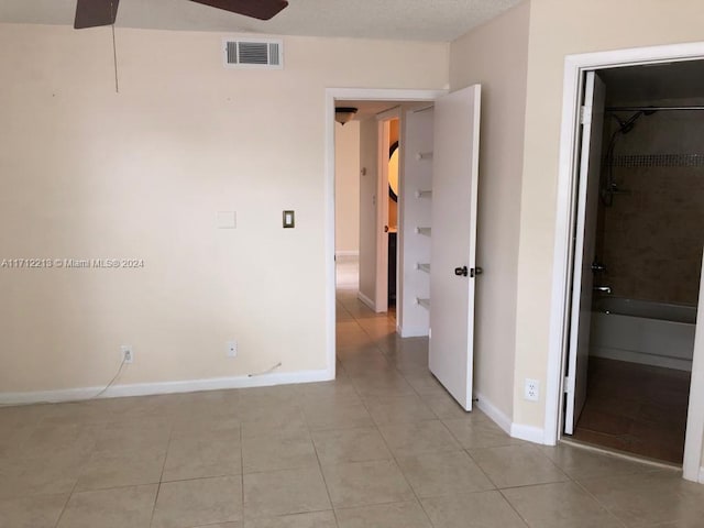 empty room featuring ceiling fan, light tile patterned floors, and a textured ceiling