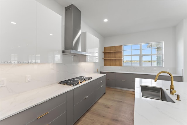 kitchen with stainless steel gas cooktop, light stone countertops, sink, and wall chimney range hood