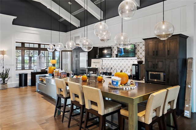 kitchen with decorative light fixtures, high vaulted ceiling, light hardwood / wood-style flooring, a kitchen island with sink, and decorative backsplash