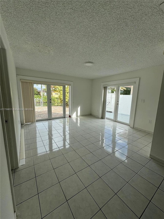 spare room featuring french doors, a textured ceiling, a healthy amount of sunlight, and light tile patterned flooring