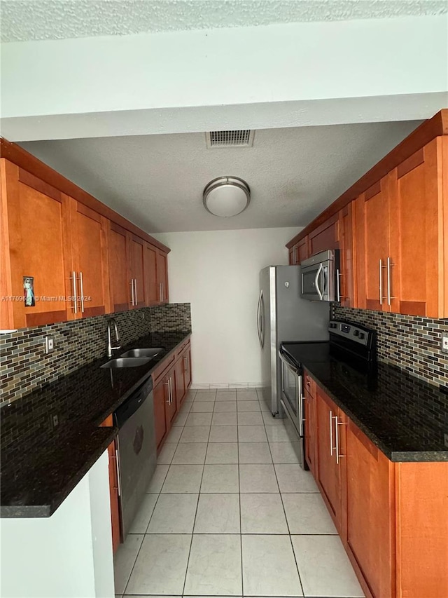 kitchen featuring appliances with stainless steel finishes, tasteful backsplash, dark stone counters, sink, and light tile patterned floors