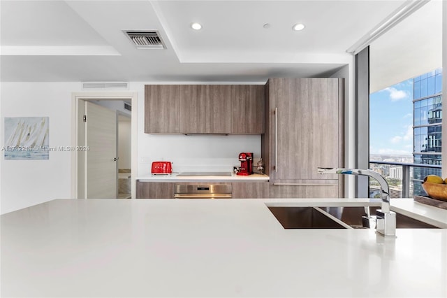 kitchen featuring oven, expansive windows, sink, black stovetop, and a tray ceiling