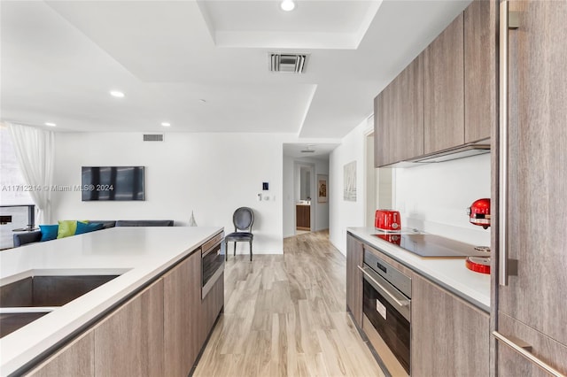 kitchen with a raised ceiling, black electric cooktop, oven, and light hardwood / wood-style floors