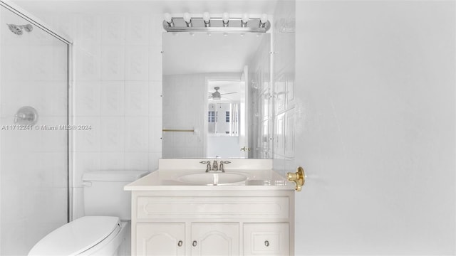 bathroom with vanity, ceiling fan, toilet, tile walls, and a shower with shower door