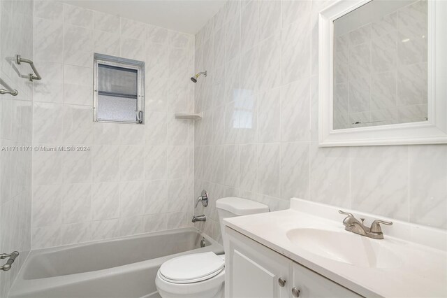 full bathroom featuring toilet, vanity, tiled shower / bath combo, and tile walls