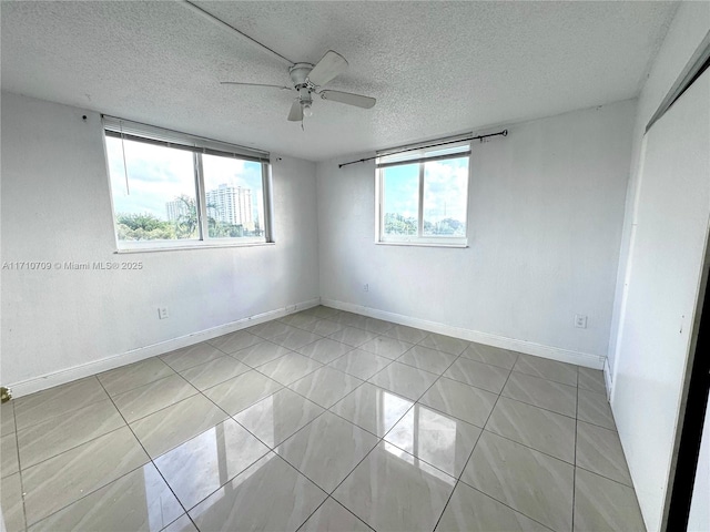 empty room with ceiling fan, a textured ceiling, light tile patterned floors, and a healthy amount of sunlight