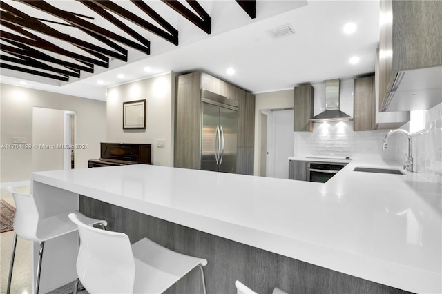 kitchen with sink, wall chimney exhaust hood, stainless steel appliances, kitchen peninsula, and a kitchen bar