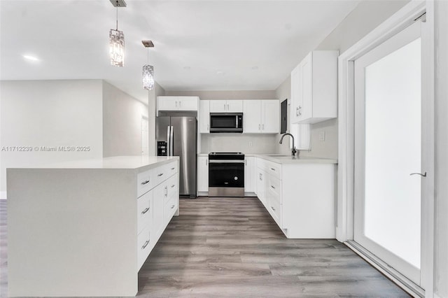 kitchen featuring white cabinetry, sink, decorative light fixtures, appliances with stainless steel finishes, and hardwood / wood-style flooring