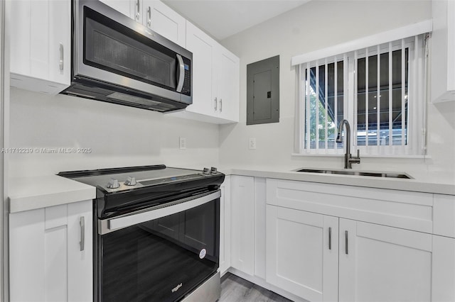 kitchen with electric panel, sink, light wood-type flooring, appliances with stainless steel finishes, and white cabinetry