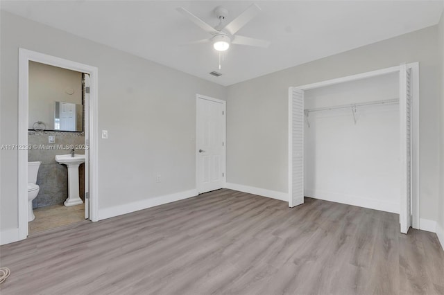 unfurnished bedroom with ceiling fan, light hardwood / wood-style flooring, ensuite bathroom, a closet, and tile walls