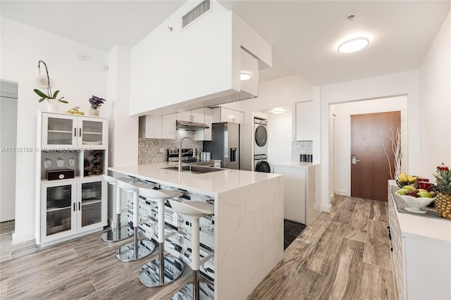 kitchen with white cabinetry, stainless steel fridge with ice dispenser, kitchen peninsula, stacked washer / drying machine, and a breakfast bar area