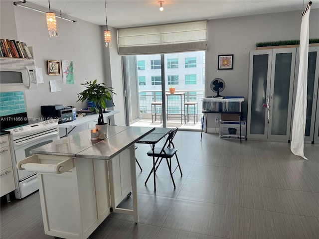 kitchen featuring white appliances, decorative light fixtures, a kitchen island, white cabinetry, and a breakfast bar area