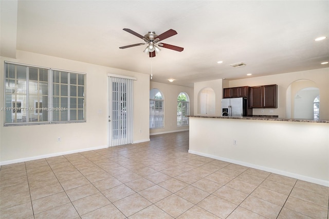 interior space featuring ceiling fan, light stone counters, stainless steel refrigerator with ice dispenser, dark brown cabinets, and light tile patterned floors