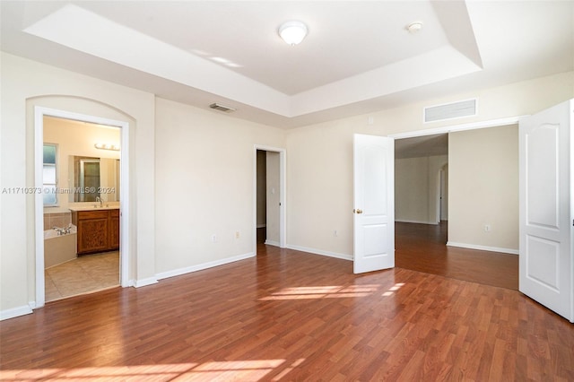 empty room featuring light wood-type flooring, a tray ceiling, and sink