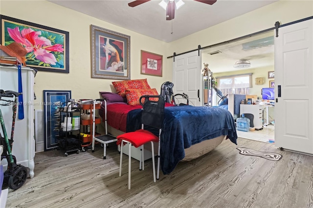 bedroom featuring hardwood / wood-style floors, a barn door, and ceiling fan