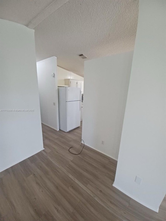 unfurnished room with wood-type flooring, a textured ceiling, and lofted ceiling