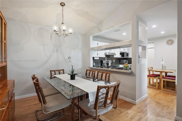 dining area with a notable chandelier, light hardwood / wood-style floors, and a textured ceiling