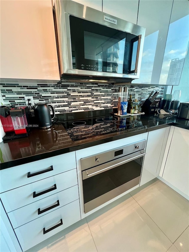 kitchen with tasteful backsplash, white cabinets, light tile patterned flooring, and appliances with stainless steel finishes