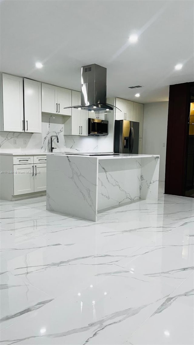 kitchen with island range hood, stainless steel appliances, backsplash, white cabinets, and light stone counters