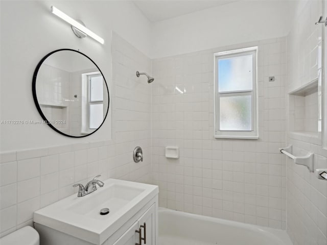 full bathroom with tiled shower / bath combo, toilet, tile walls, and vanity