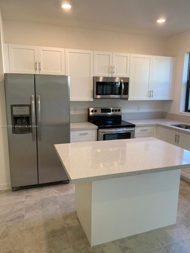 kitchen featuring light stone countertops, a center island, white cabinets, and appliances with stainless steel finishes