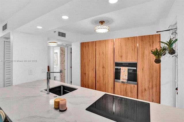 kitchen featuring sink, stainless steel oven, light stone counters, and black electric stovetop