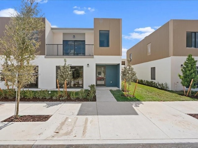 view of front of home with a balcony, a front yard, and stucco siding