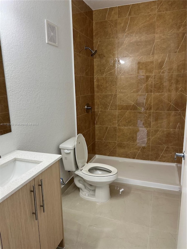 bathroom with tile patterned floors, vanity, toilet, and a tile shower