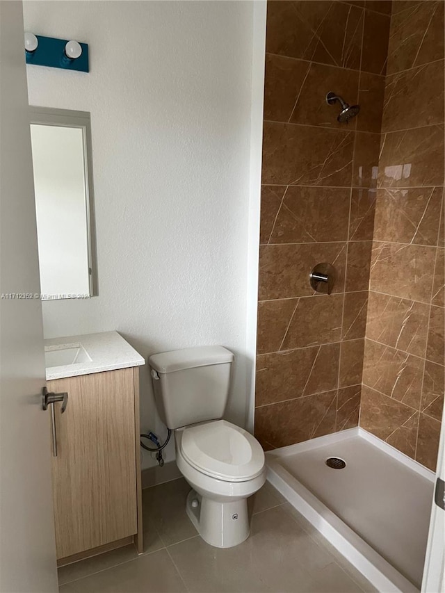 bathroom with tile patterned flooring, a tile shower, vanity, and toilet