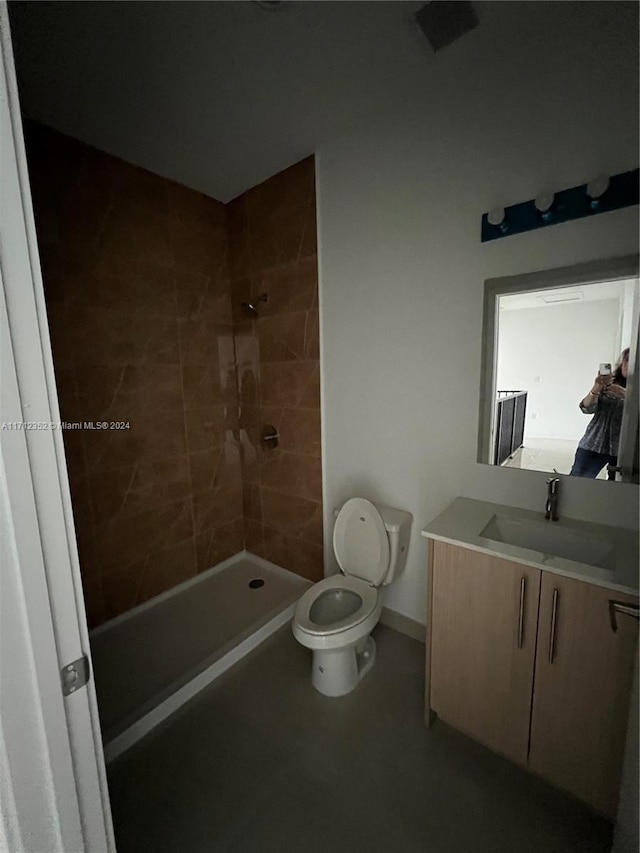 bathroom featuring a tile shower, vanity, and toilet