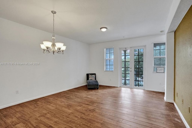 empty room with hardwood / wood-style floors, french doors, and a notable chandelier