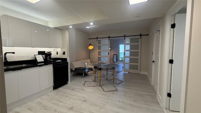 kitchen with white cabinets, black dishwasher, a barn door, and sink