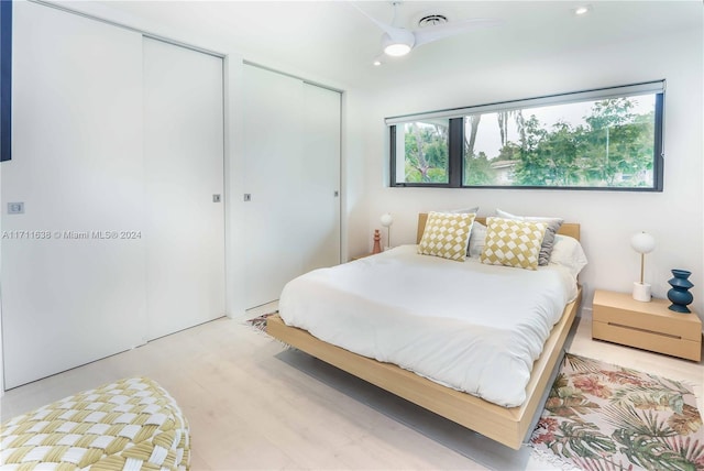 bedroom featuring ceiling fan, multiple closets, light hardwood / wood-style flooring, and multiple windows