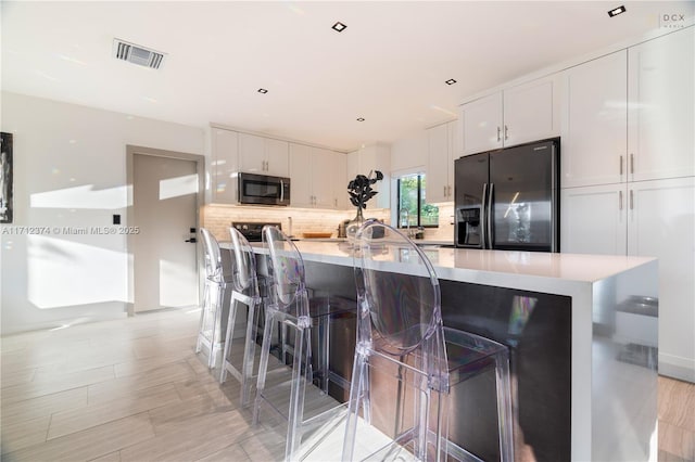 kitchen with black fridge, white cabinetry, a breakfast bar area, and backsplash