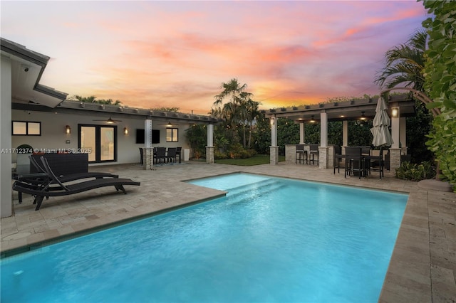 pool at dusk with a bar, ceiling fan, an outdoor hangout area, and a patio