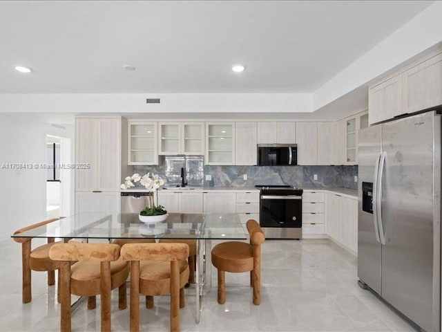 kitchen featuring a sink, visible vents, appliances with stainless steel finishes, decorative backsplash, and glass insert cabinets